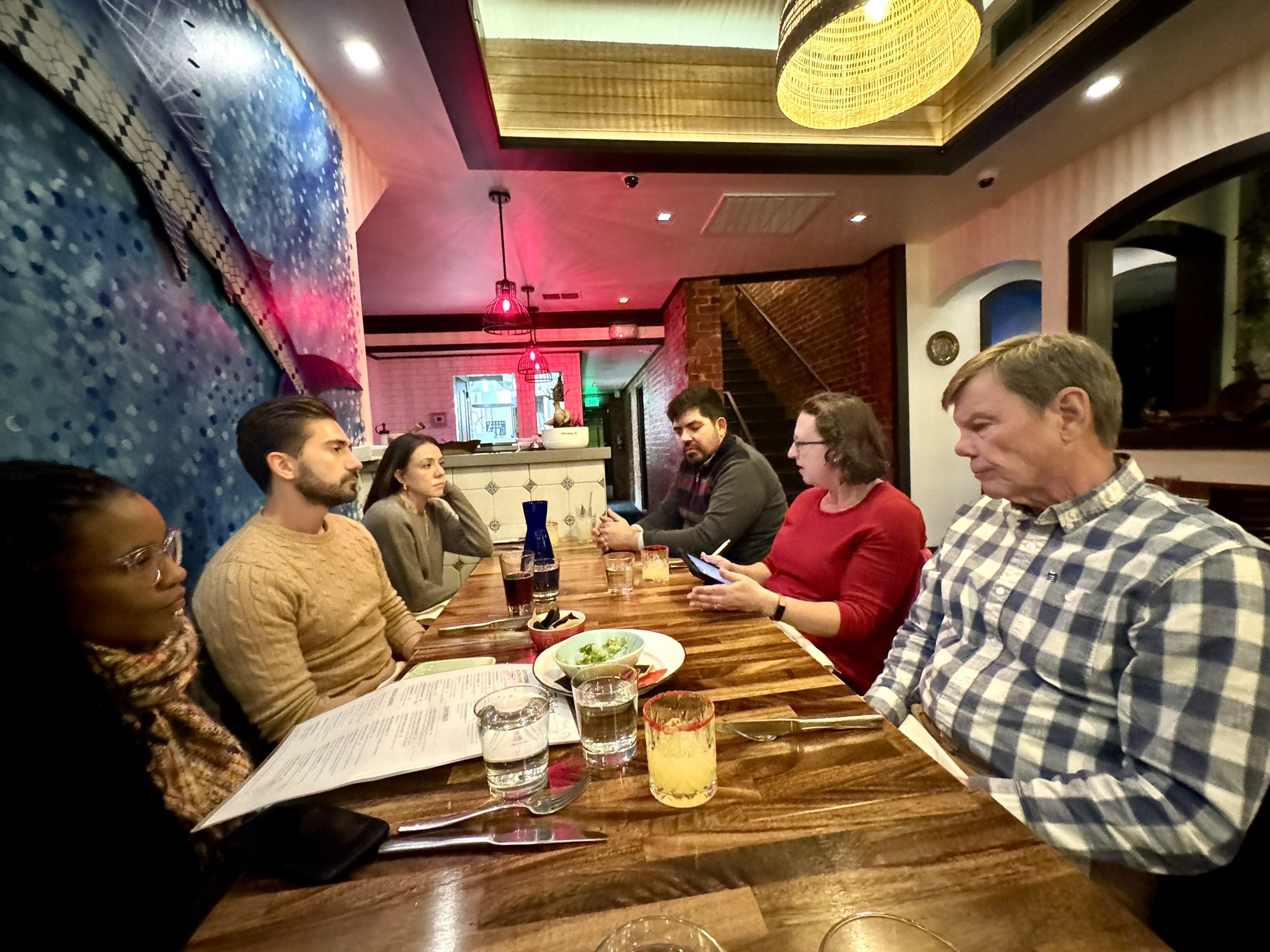 Six people are seated at a restaurant table in conversation.